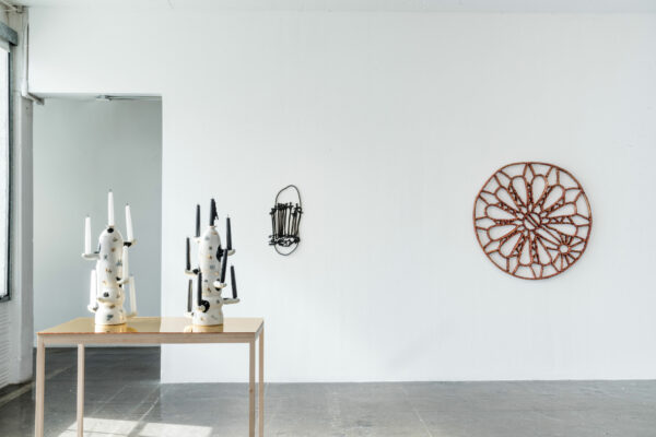 Installation view of black and white porcelain candle holders on the left and sculptural work on the wall.