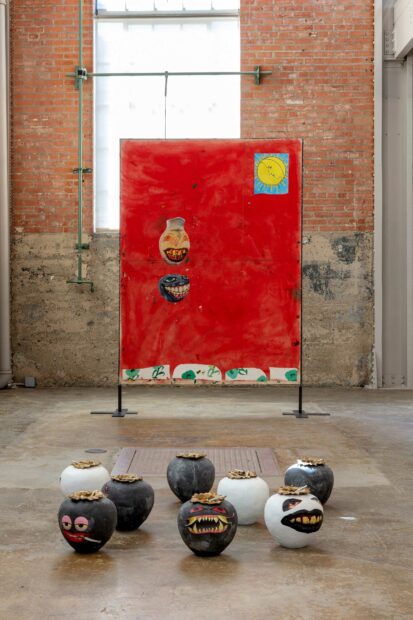 Installation view of a red painting and vases with snarling mouths, and three dimensional black and white vases on the floor in front