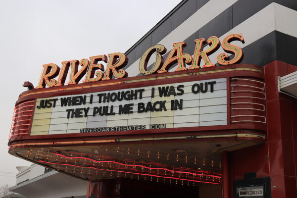 A photograph of the marquee sign for the River Oaks Theatre. Above the sign are large neon letters that spell, "RIVER OAKS." On the marque the words read, "Just when I thought I was out they pull me back in."