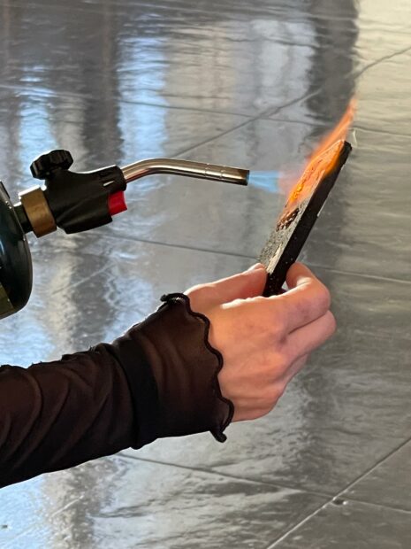 Photo of an artist burning a piece with a handheld blow torch