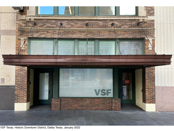 A color photograph of the VSF Texas storefront located in downtown Dallas. The brick building has a large display window in the front which is flanked by two recessed doors. 