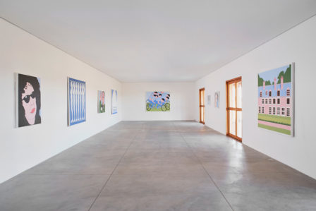 A photograph of the interior of a gallery. Eight paintings by John Wesley hang on the walls of the gallery.