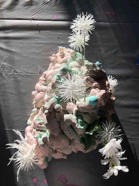 A photograph of a work in progress by Alyssa Danna. The piece is a small organic sculpture which includes faux flowers.