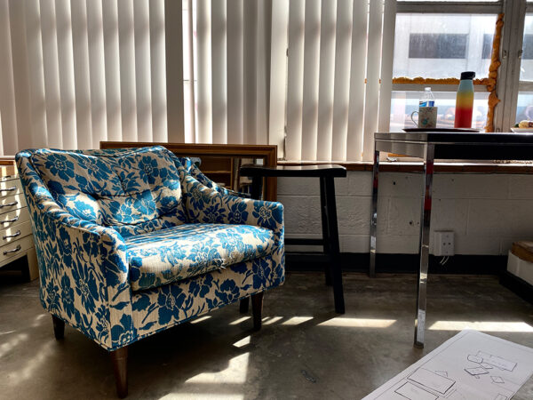 A photograph of the interior of Carol Ivey's studio at Arts Fort Worth. The image shows a blue and white floral patterned chair sitting in front of a window.