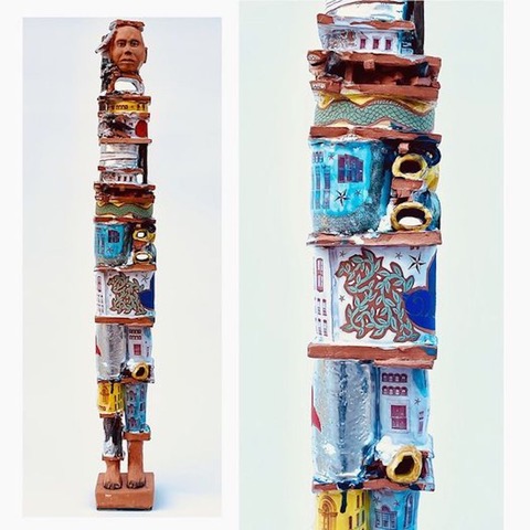 A photograph of a tall thin sculpture by Clara Hoag. The sculpture depicts a human head at the top and a human feet at the bottom, but the pieces in between architectural elements.