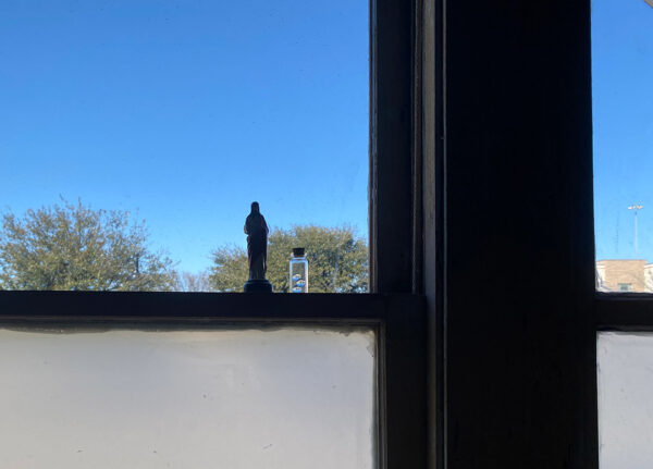 A photograph of a small Jesus figure and a vial of glass beads on the window in Michelle Cortez Gonzales' studio