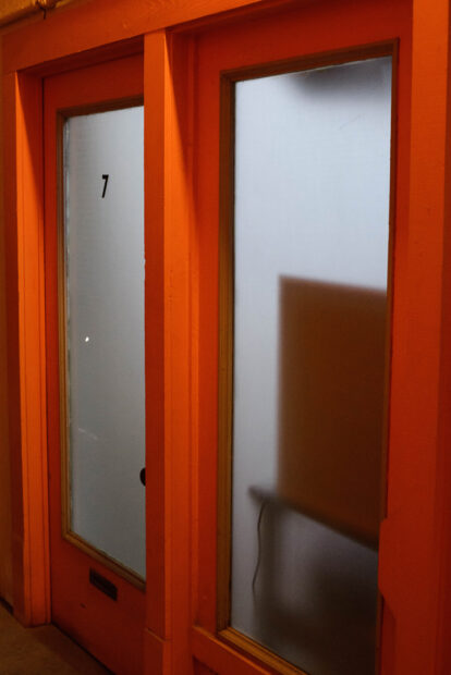 The door of the studio of Anthony Francis which shows frosted glass and a red-orange door frame. The number '7' is on the glass, indicating the studio number.
