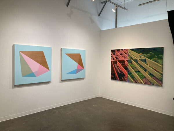An image of three paintings displayed on the white walls of a gallery. On the left are two paintings each with a geometric design centered on a blue field. On the right is a large scale painting of pieces of wood. 