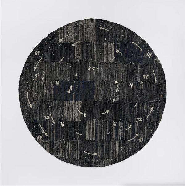 A fabric work by Jamal Cyrus. A large circular piece made from black and gray denim. Cotton thread is used to make arrows which point in a counterclockwise direction and have numbers next to them.