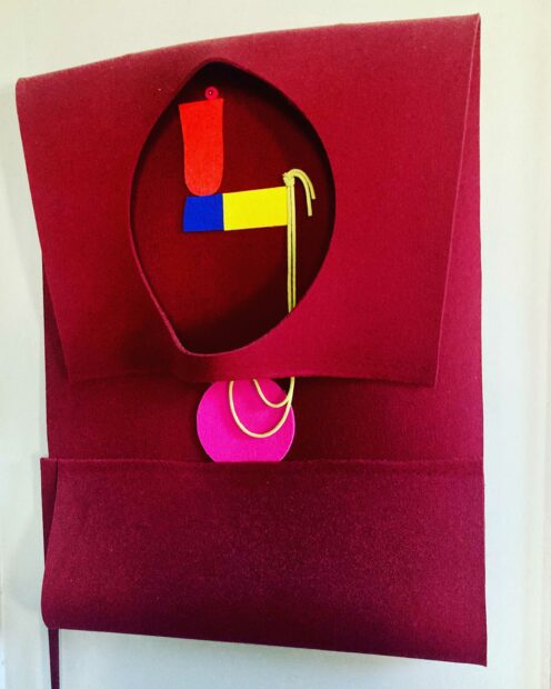 A work of red felt folded over to reveal a round cutout and shapes of yellow, red, pink and orange under
