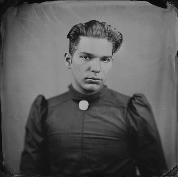 A black and white tintype photograph of a young person wearing a top or dress with puffy sleeves. 