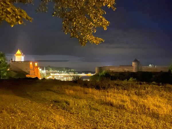 Photo of a brightly lit Narva on the European side of the Narva River, and Russia on the left in near darkness at night.