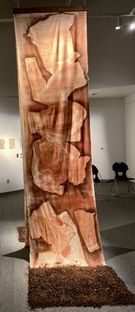 Vertical piece hanging from ceiling to floor with ghost impressions of clothing