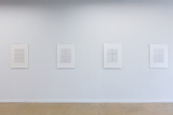 Four works on paper in a row on a white wall. The works of paper are drawings of black and white grids of DNA