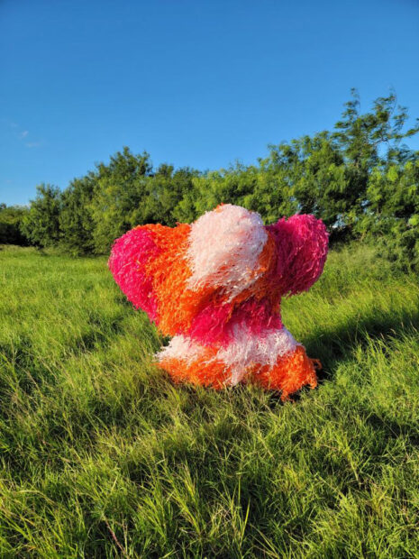 A dancer wearing a costume made of white, orange and pink Piñata paper dancing in a green field