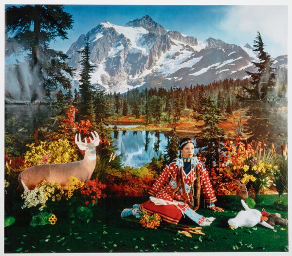 Image of the artist in Native American dress sitting in a fake, contrived landscape