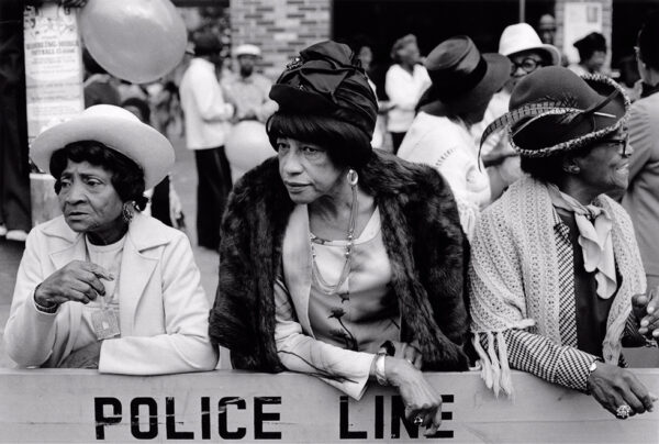 A black and white photograph of three African American women at a parade in Harlem, New York. The photograph is by Dawoud Bey.