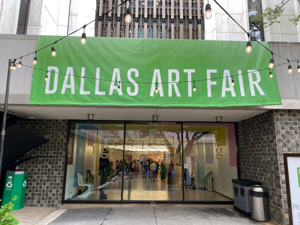 A photograph of the outside of the Fashion Industry Gallery with a large green banner with white text that reads, "Dallas Art Fair."