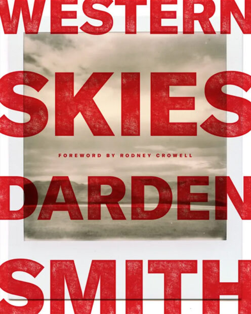 A photograph of the book cover of "Western Skies," by Darden Smith. The cover is filled by an enlarged black and white polaroid photograph and has large red text that reads, "Western Skies Darden Smith." Smaller text in the center reads, "Foreword by Rodney Crowell."