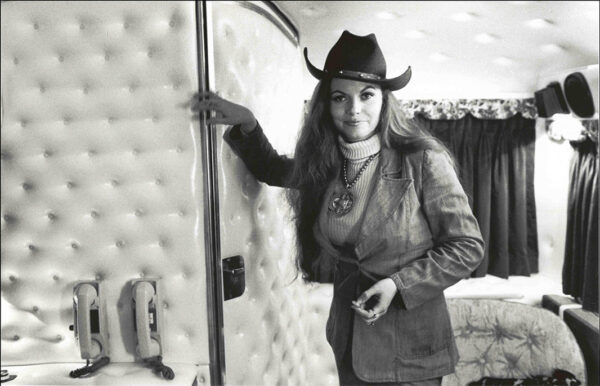 A black and white photograph by Henry Horenstein of Jeannie C. Riley. She is standing inside a tour bus and wearing a black cowboy hat, a turtle neck, and a blazer. 