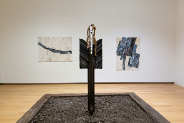 Image of a sculpture of a manipulated saxophone in the foreground and two dimensional works in the background