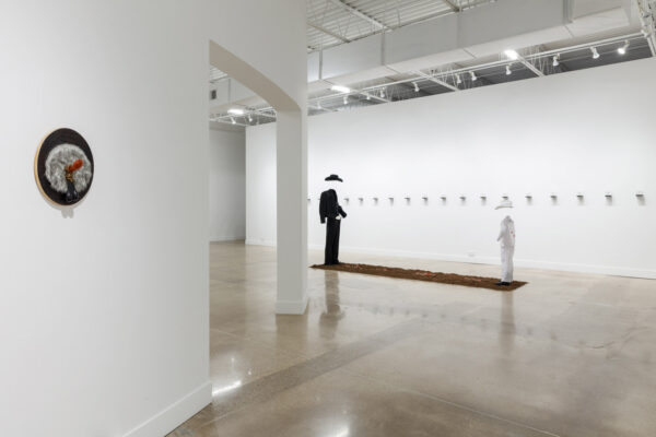 An interior view of a gallery with white walls and a curved wall with and opening on the left side of the image. Sculptures sit on the wall and on the floor.