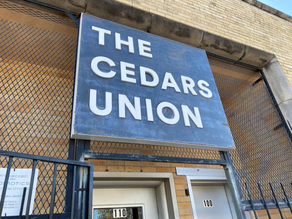 A photograph of the outside exterior of The Cedars Union building with the sign displayed prominently.