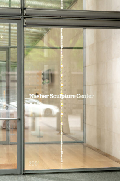 A photograph of a long thin hanging sculpture by Tamara Johnson in the window of the Nasher Sculpture Center.
