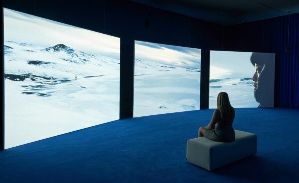 Installation view of a large three-channel video piece with an individual in the room