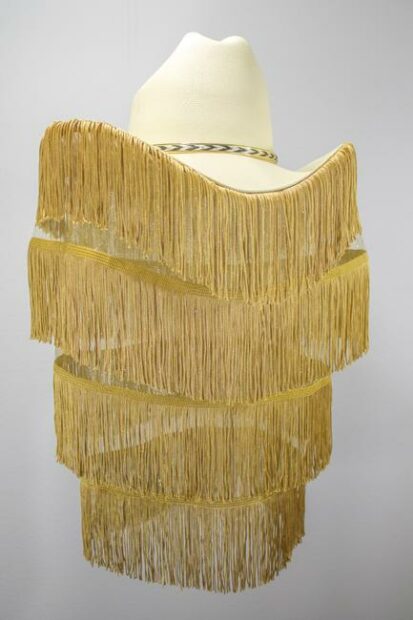 A sculpture by José Villalobos featuring a white cowboy hat with four tiers of gold fringe hanging from it.
