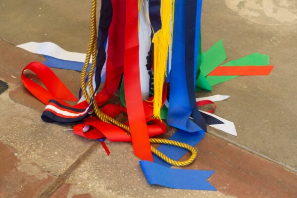 A group of fabric ribbons hangs from above and coils on the floor. There are tassels, cords, and striped ribbons as well.