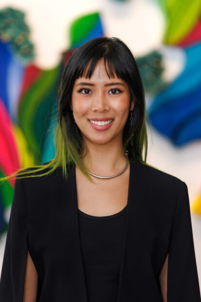 A photograph of Cat Yue by Jay Marroquin. Yue wears a black blazer and black shirt. She looks directly into the camera with a smile.
