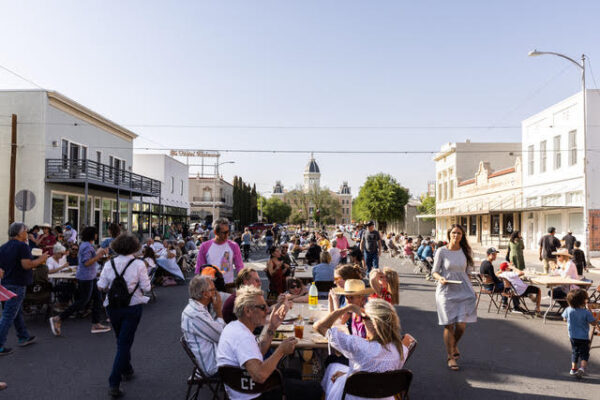 A photograph of a large crowd of people eating at tables set up on a temporarily closed street in downtown Marfa.