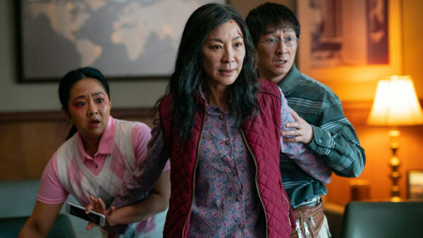 A still screen of "Everything Everywhere All At Once". From left to right, Stephanie Hsu, Michelle Yeoh, and Ke Huy Quan stand in an alarmed state with a lamp alight on their right