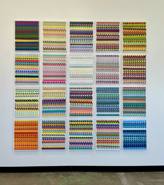 Installation view of vertical paintings hanging in a grid pattern on a wall