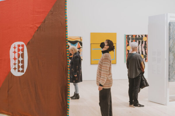 Image of visitors looking at two dimensional objects in a white cube gallery space