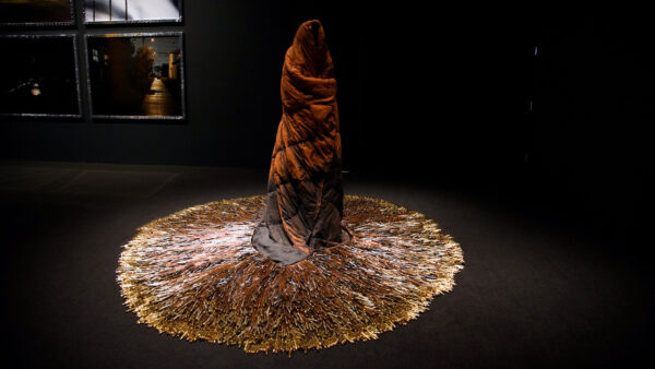 A sculpture of a person wrapped in a blanket standing atop a rug of bullet casings