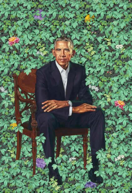 Portrait of Barack Obama sitting in a chair in front of a backdrop of lush green foliage