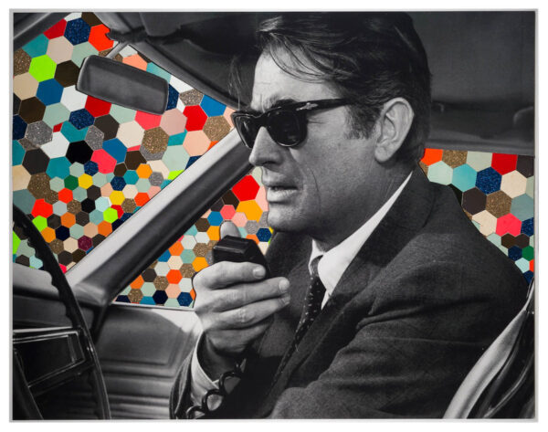 Photograph of a man sitting in a car and holding a radio. He is speaking into the radio, and wearing a suit and sunglasses. The background is many hexagonal colorful shapes.