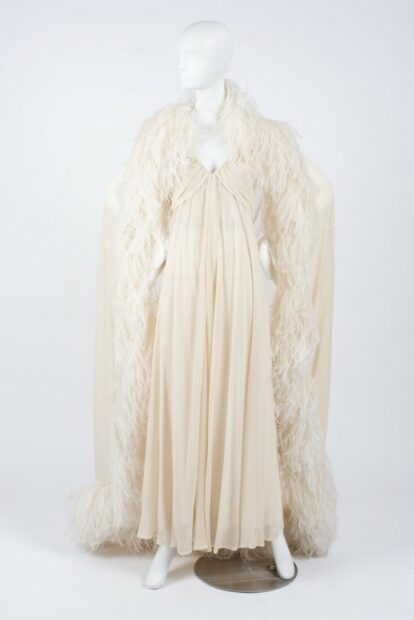 A dress designed by Hubert de Givenchy, made out of cream-colored chiffon and adorned with a cape that has ostrich feathers lining its edges.