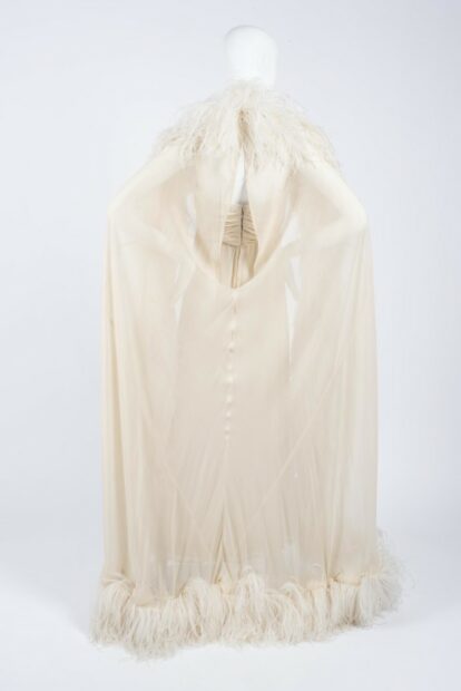 A dress designed by Hubert de Givenchy, made out of cream-colored chiffon and adorned with a cape that has ostrich feathers lining its edges.
