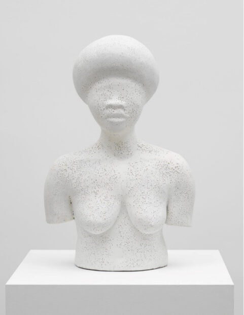 A white glazed stoneware sculpture by Simone Leigh of a nude female figure. The figure is shown from the waist up. There are no details to the figure's eyes.