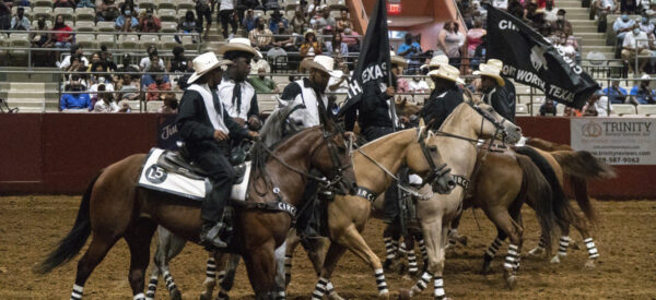 A photograph of eight Black cowboys riding horses in an arena.