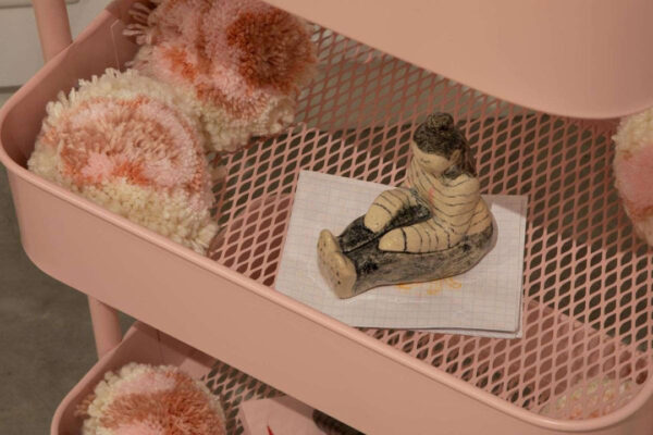 A detail of Chelsea Clarke's Self-Soothe featuring a small sculpture of a girl seated on a pink cart.