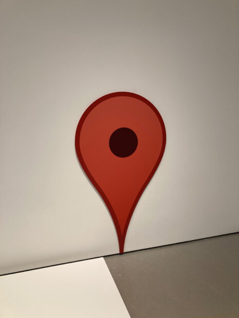 An oversized digital print of the Google Maps pin designed by Jens Ellstrup Rasmussen is pasted flush against the wall, pointing to the floor.