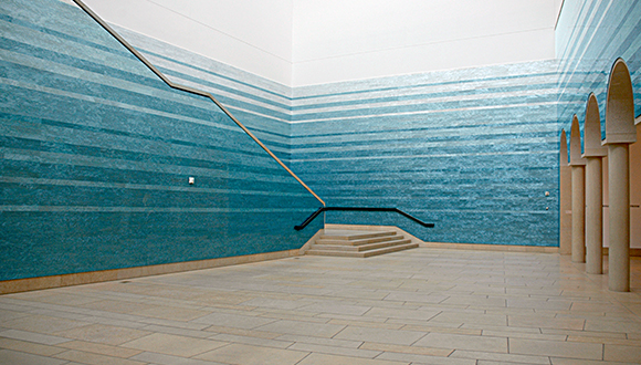 Photo of the interior of the central atrium of the Blanton Museum of Art with a gradient blue installation piece emulating a pool of water