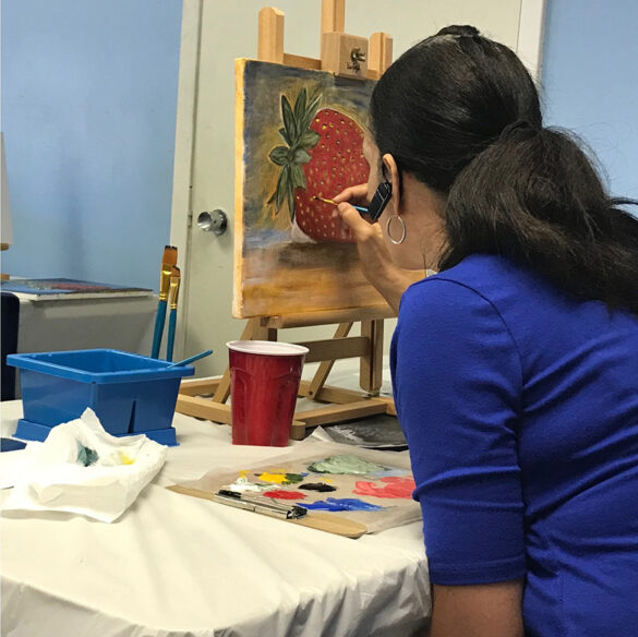 A participant of the Bihl Haus Arts program, "Forward, Arts!" works on a painting of a strawberry on tabletop easel.