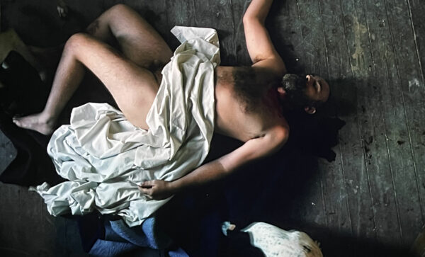 Video still of a man lying on the floor covered by a sheet