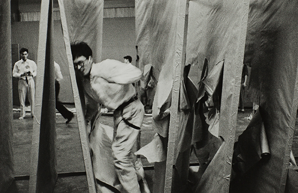 A black and white photograph of an artist tearing through large artworks.