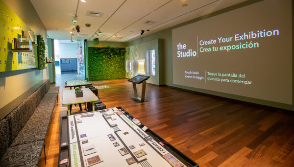 An installation photo of a newly designed interactive space within the McNay Art Museum. The space features a large screen, tables with activities, and works of art.